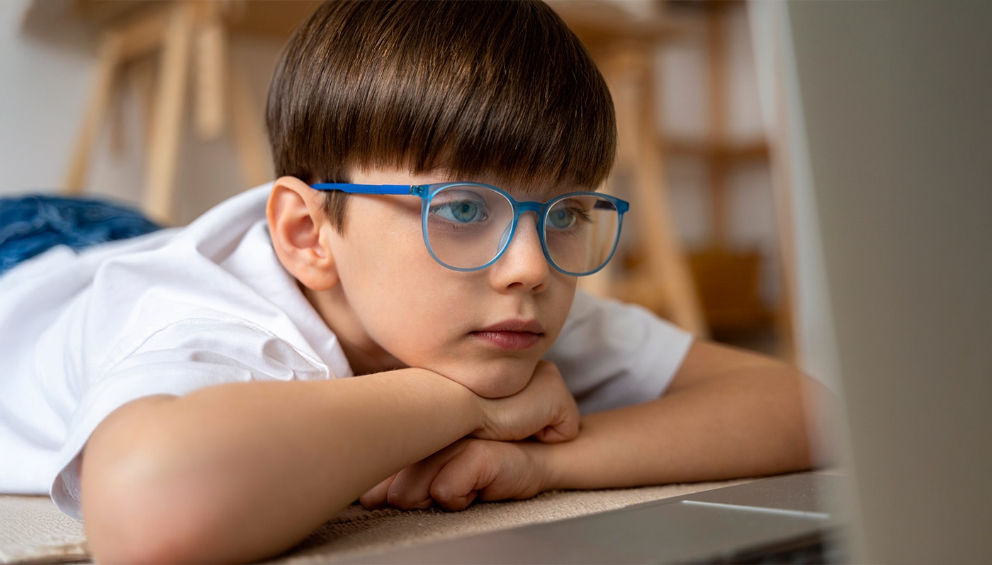 kleiner Junge kurzsichtig mit Brille der Filme auf dem Laptop anschaut